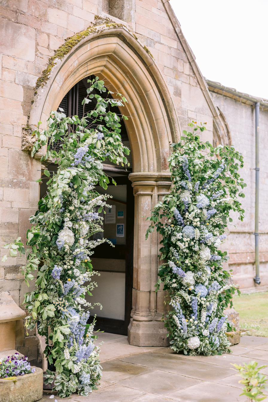 Blue and white floral arch framing the church doorway, Lucia and Alex's marquee wedding in Rutland