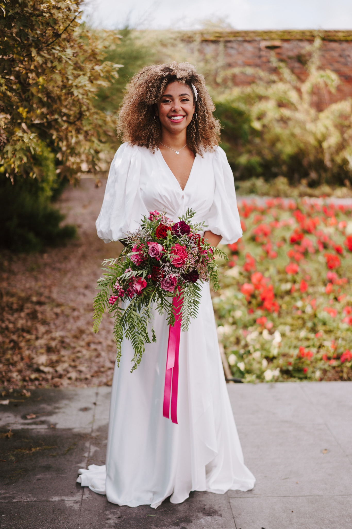 Bride with a vivid pink and raspberry bouquet in the walled garden, Dionne and Alistair's manor house wedding in Lincolnshire