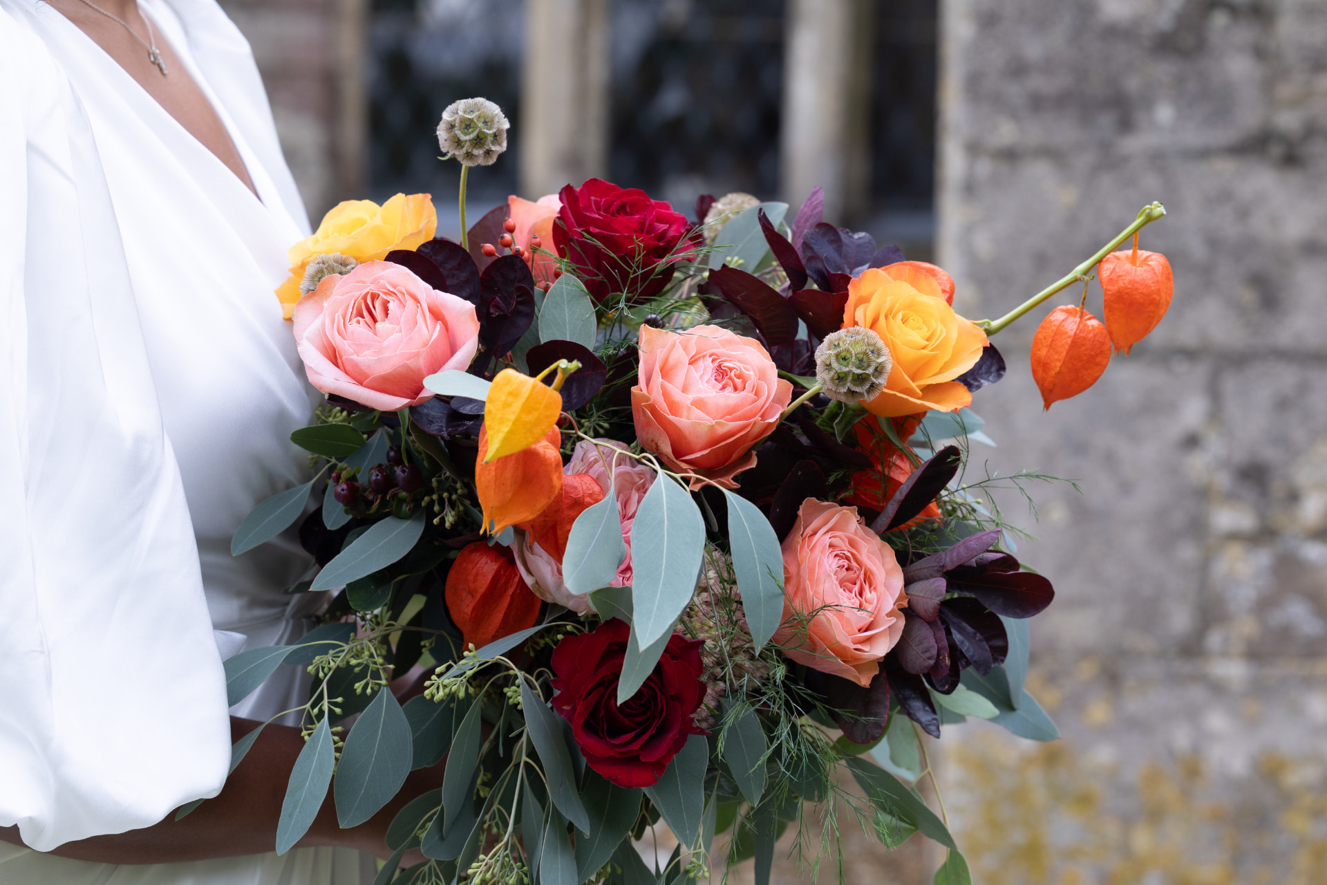 Autumn bridal bouquet with roses and physalis against honey coloured stone, Dionne and Alistair's manor house wedding in Lincolnshire