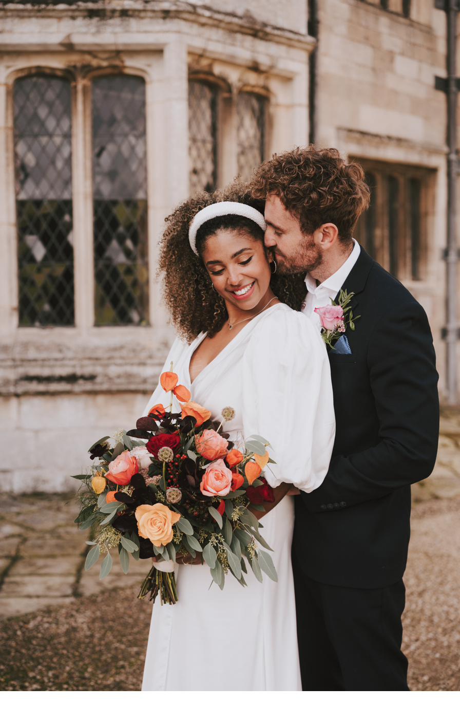 Bride with a coral and burgundy autumn bouquet held by her groom, Dionne and Alistair's manor house wedding in Lincolnshire