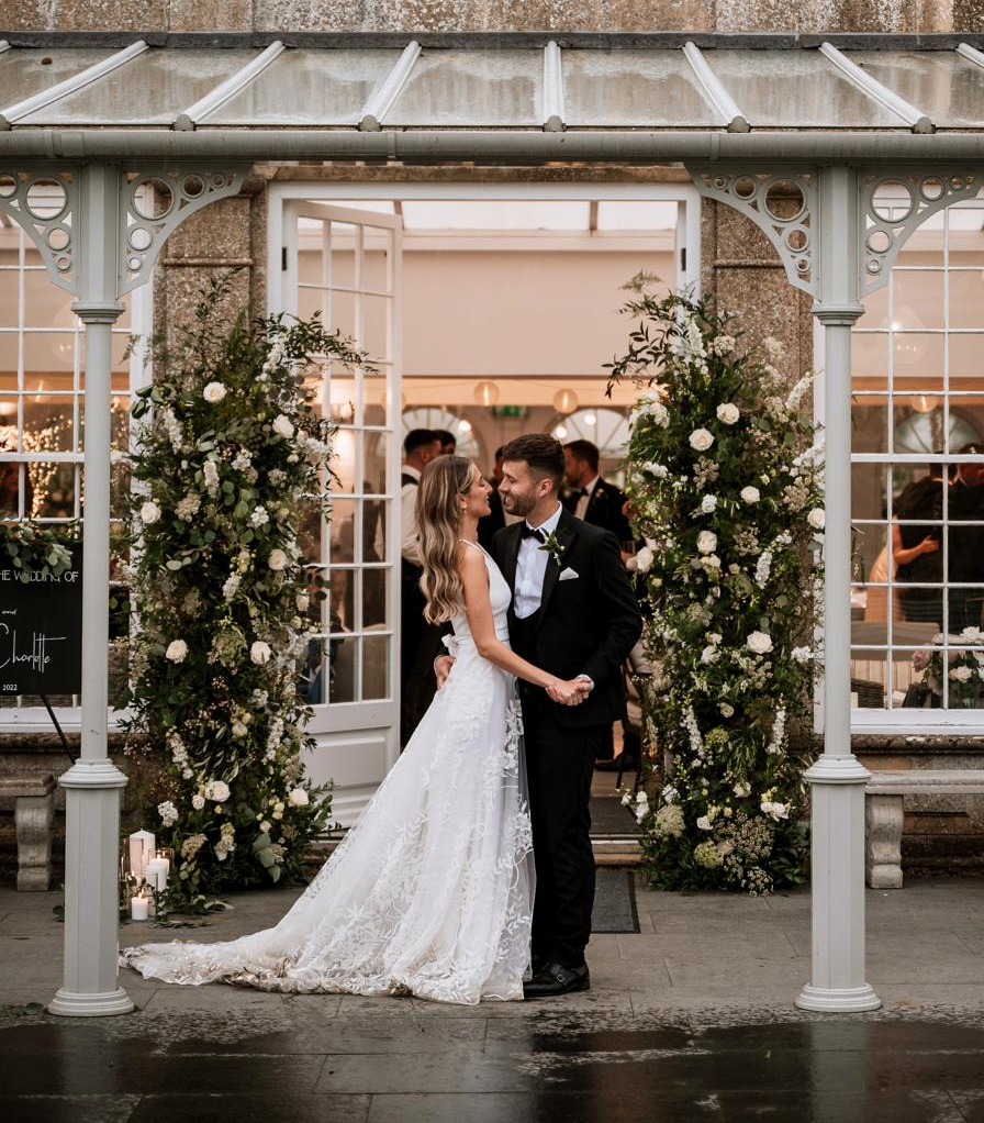 Bride and groom at dusk beneath the floral entrance, Joe and Charlotte's orangery wedding in Lincolnshire